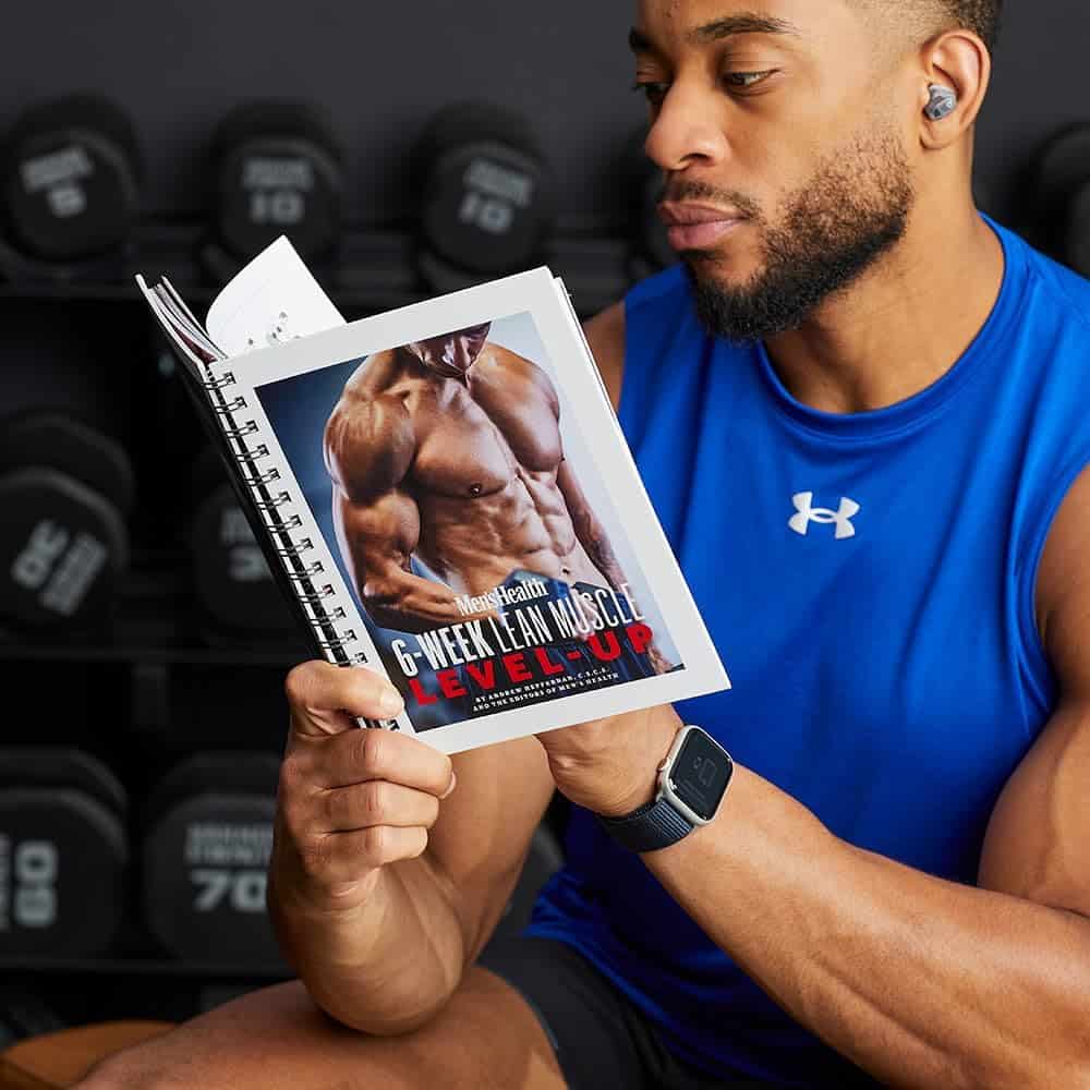 Man holding a fitness book with gym equipment in the background