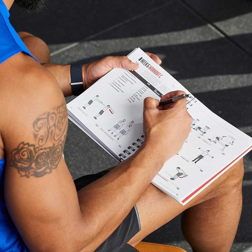 Person holding a workout book with exercise illustrations outdoors.