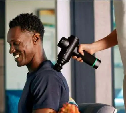 Person using a massage gun on another person's back in an indoor setting