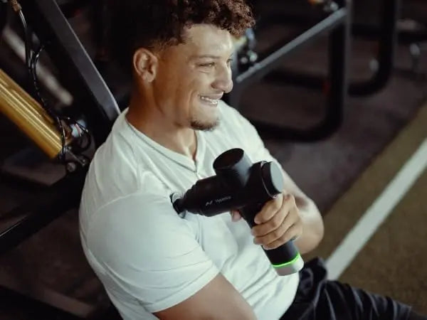 Man using a massage gun in a gym setting