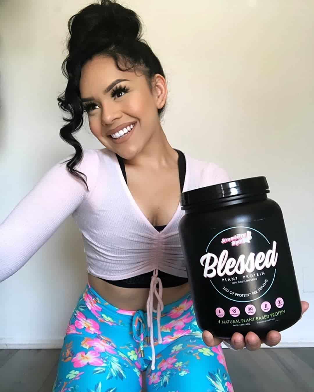 Woman holding a 'Blessed' protein powder container against a neutral background