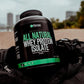 Protein supplement container labeled 'All Natural Whey Protein Isolate' on a black bag with a blurred outdoor background.