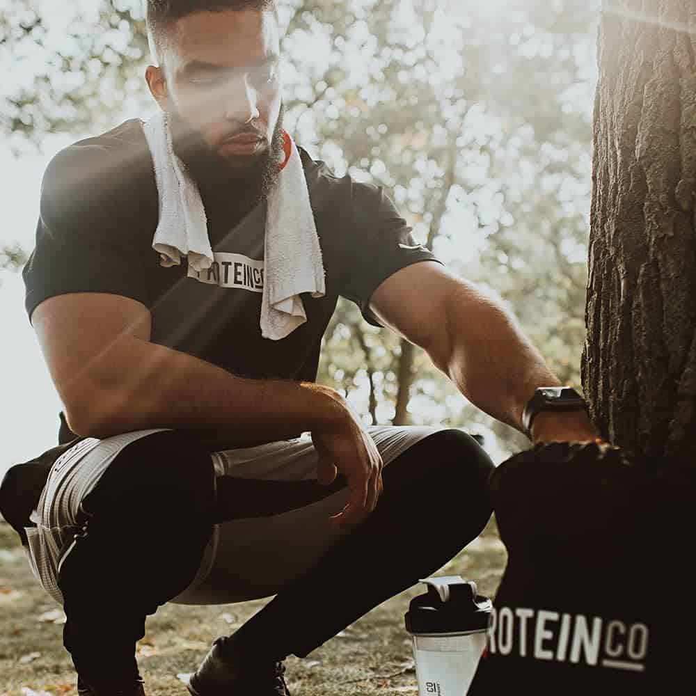 Man in athletic wear with a towel and protein powder, outdoors.