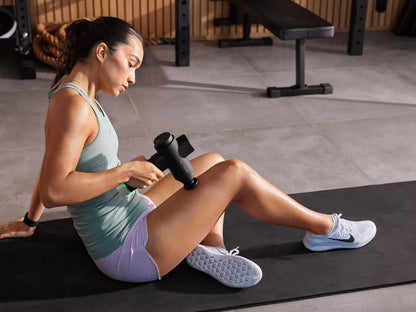 Woman using a massage gun on her leg in a gym setting