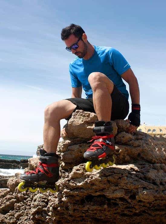 Person sitting on rocks wearing rollerblades with a clear blue sky and ocean background