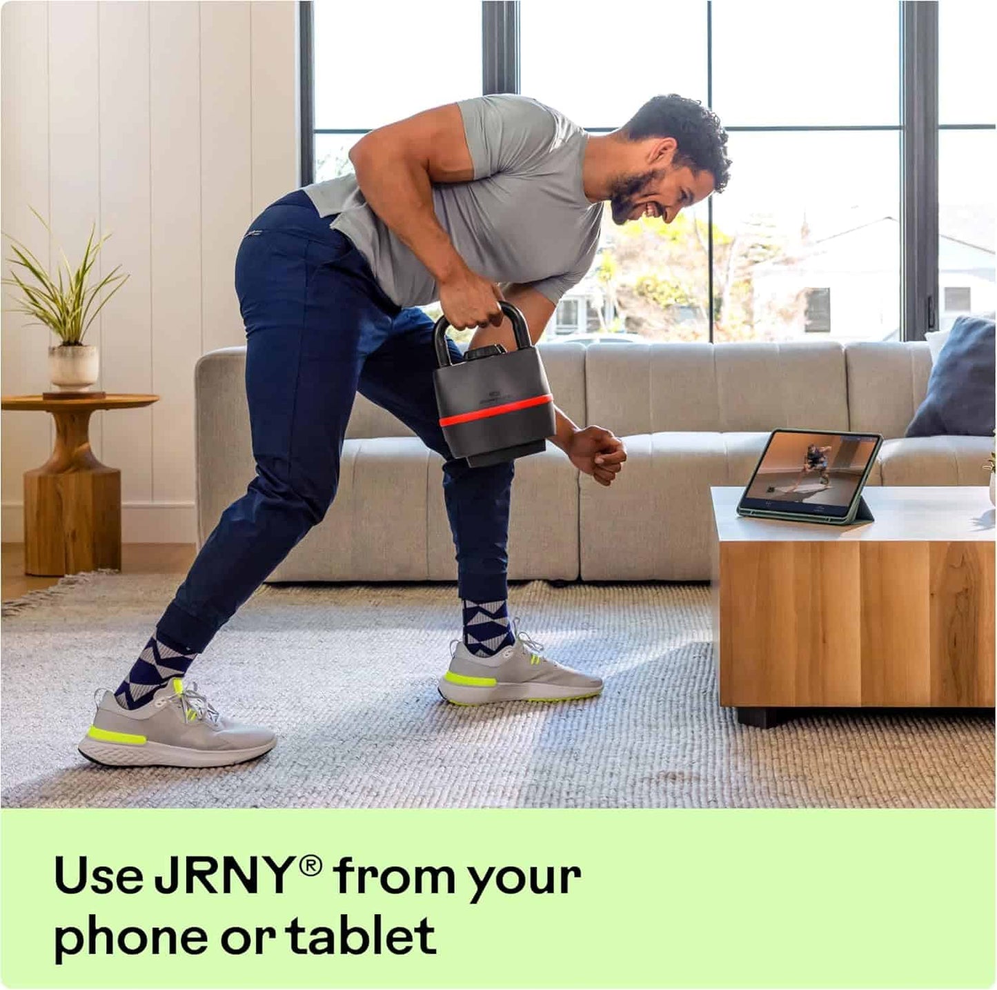 Man exercising with dumbbells in a living room using a tablet for guidance, with text promoting JRNY app.