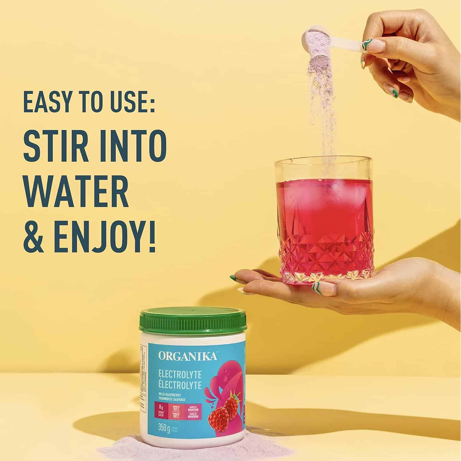 Person pouring a drink mix into a glass with a container of Organika electrolyte powder on a yellow background.