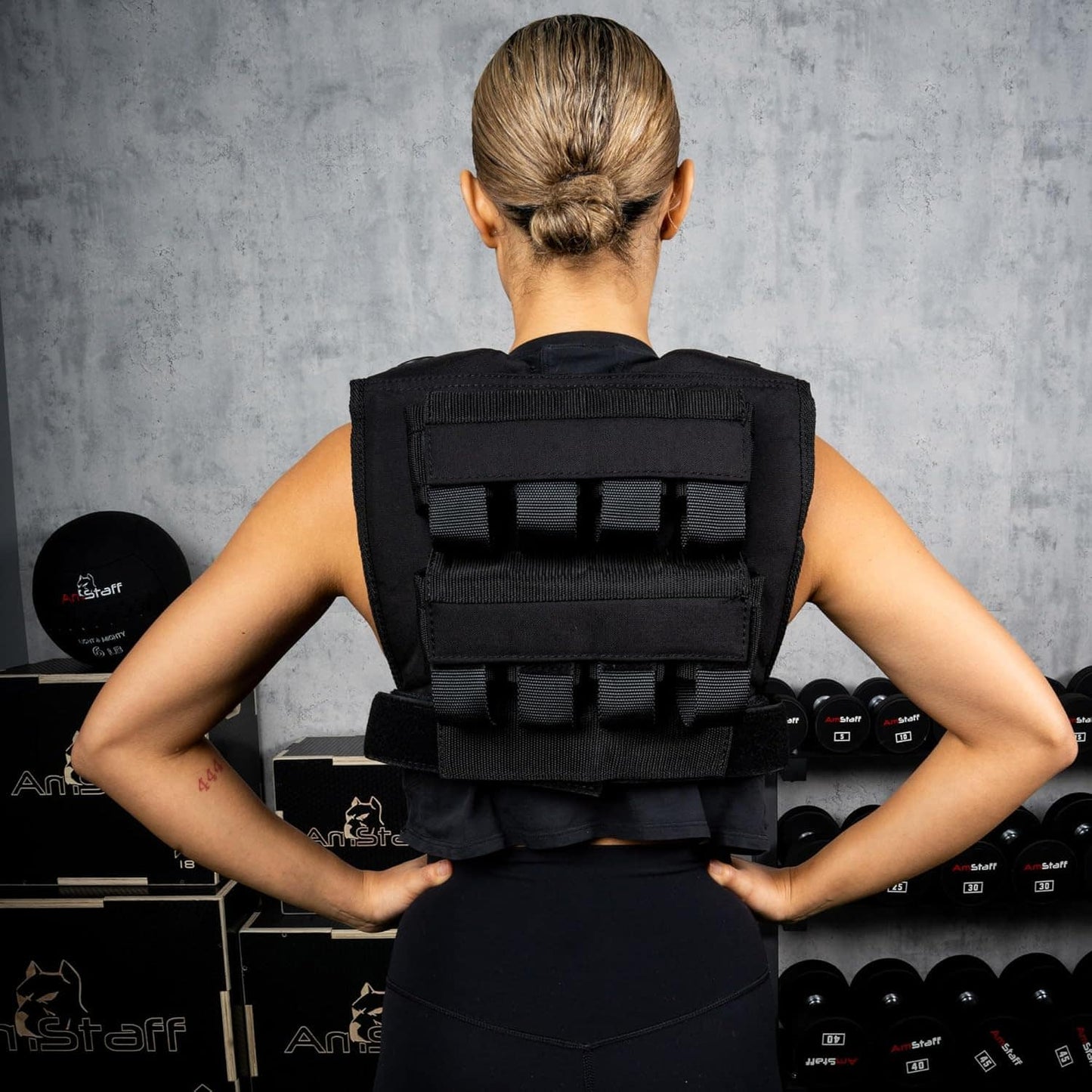 Person wearing a black weighted vest in a gym setting