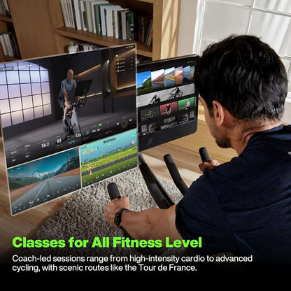 Person using a stationary bike with multiple screens displaying fitness classes in a home setting.